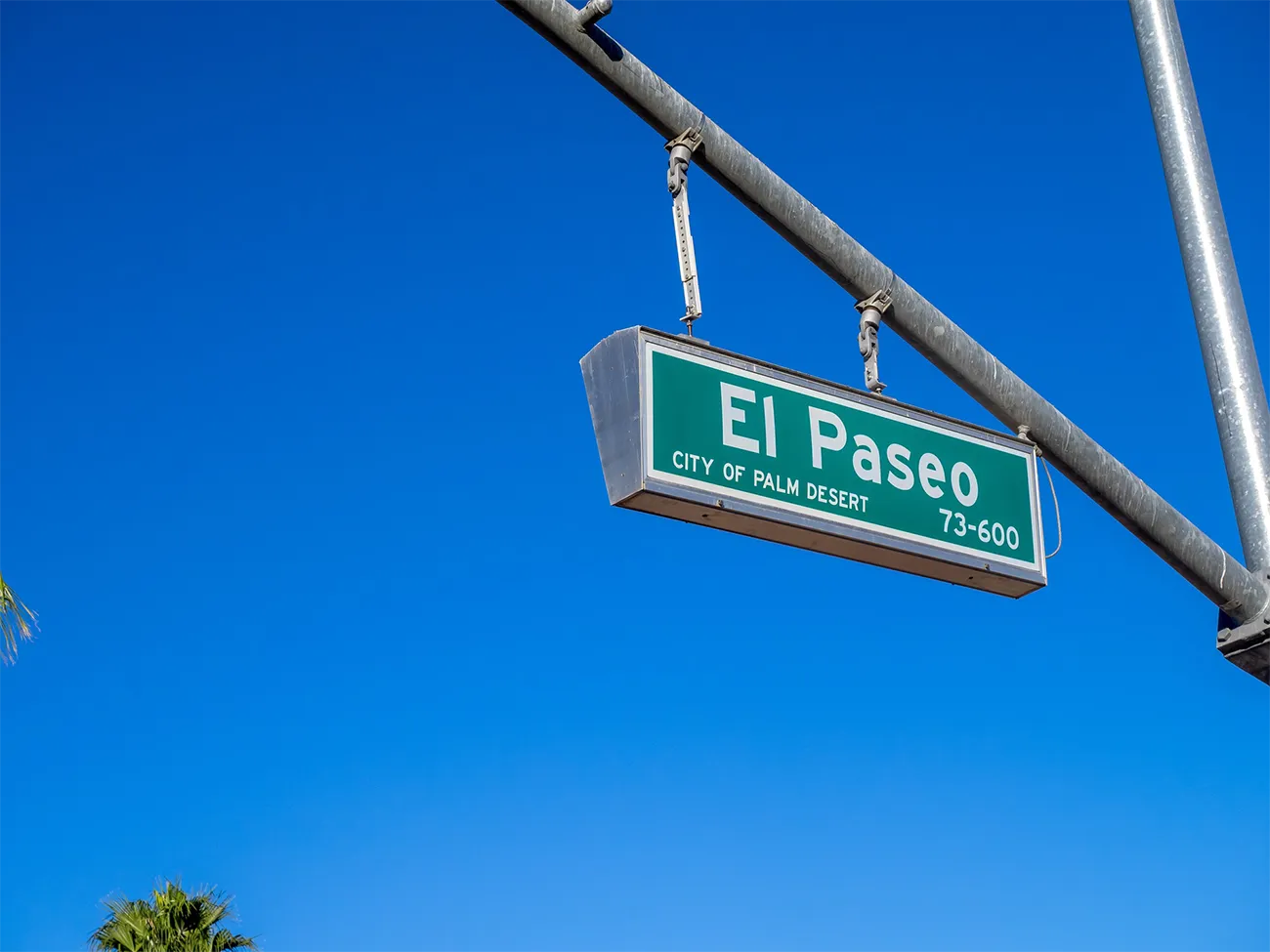 A street sign for El Paseo against a clear blue sky.