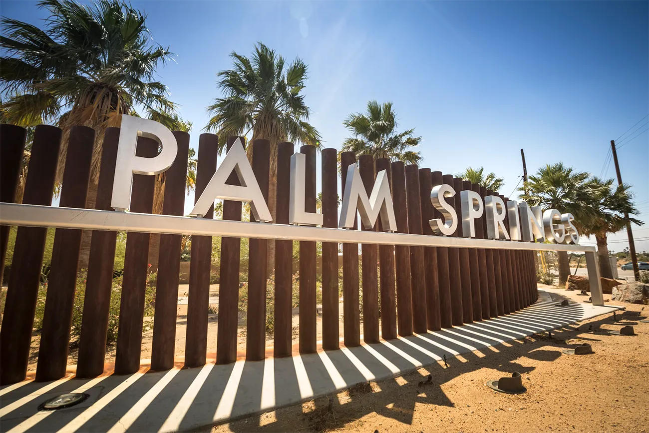 The entrance sign to Palm Springs, featuring large letters spelling out 'Palm Springs' with palm trees in the background.