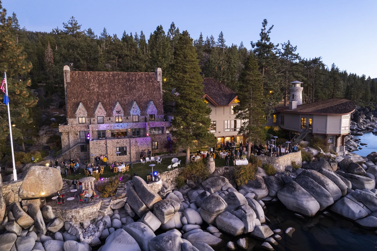 Guests mingling outside Thunderbird Lodge during an event, with the historic stone building and forested lakefront setting in view