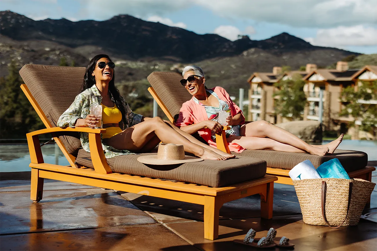 A group of women enjoying a meal outdoors on deck chairs with a scenic mountain view in the background at The Welk.