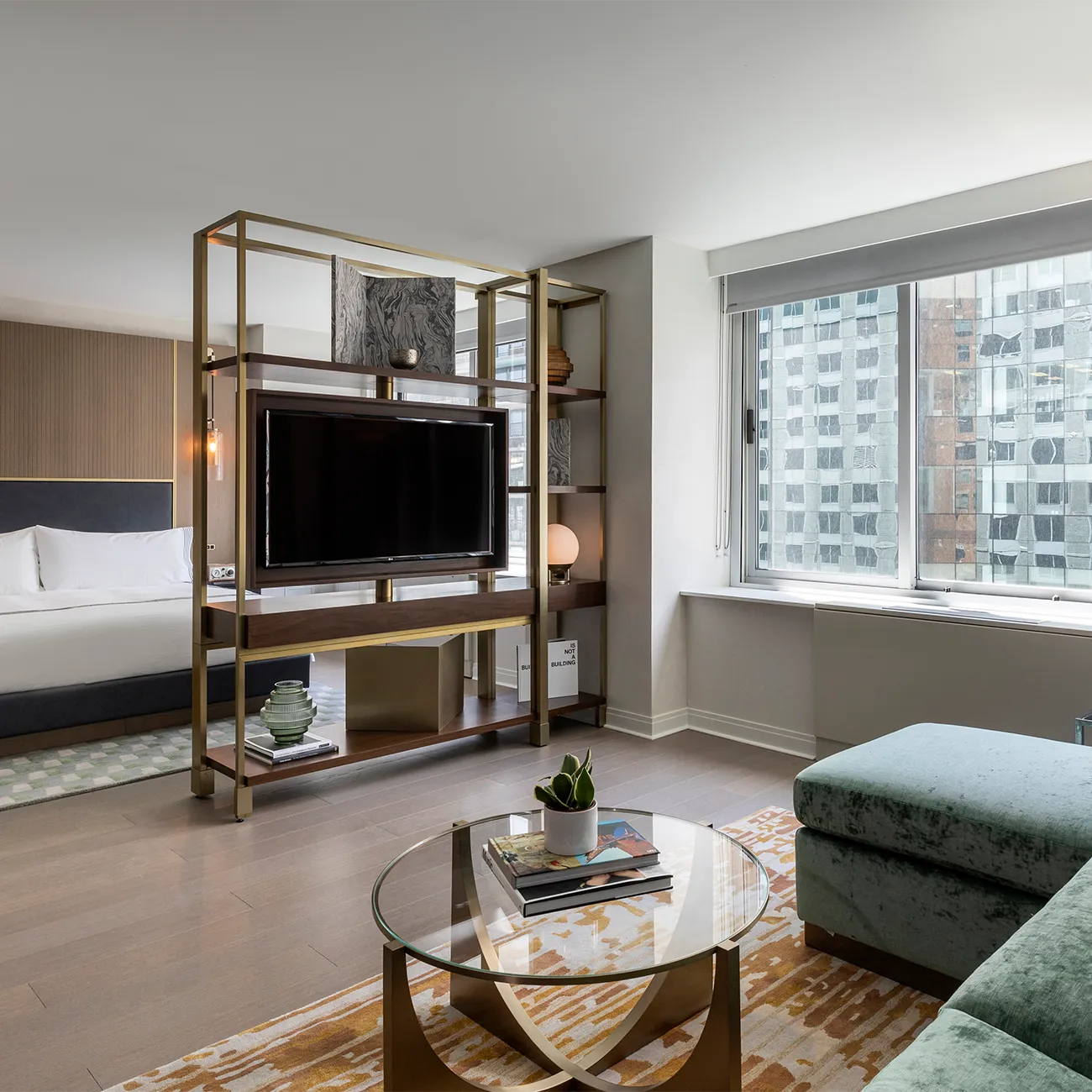 An expansive studio suite with sleeper sofa modern guest room with a large window allowing natural light to fill the space, featuring sectional sofa, coffee table, and wall-mounted TV.