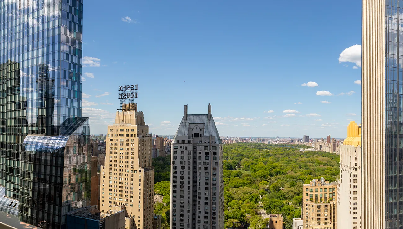 A cityscape with tall buildings and a large park in the background under a clear sky.