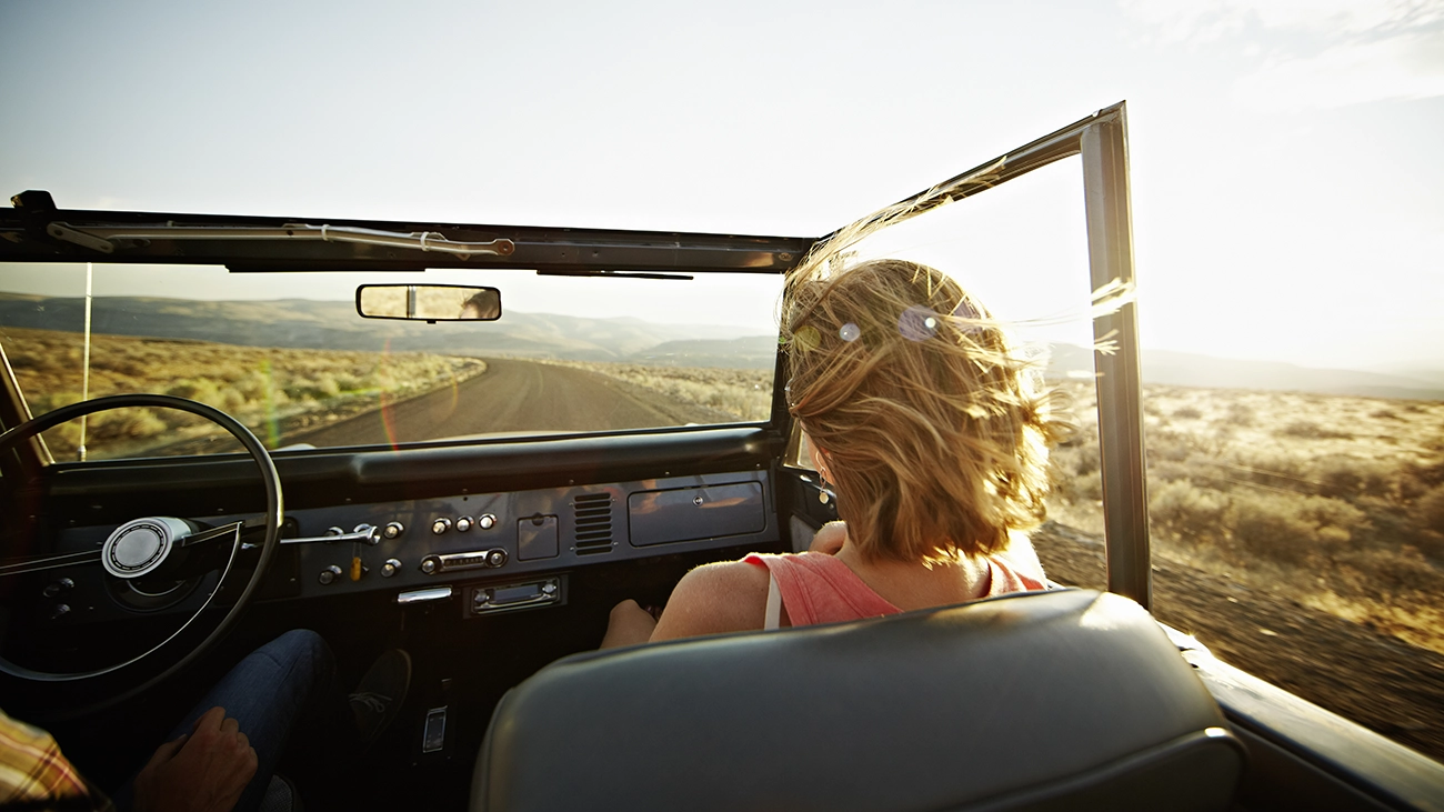 Woman riding in a convertible car on a sunny day, her hair blowing in the desert wind