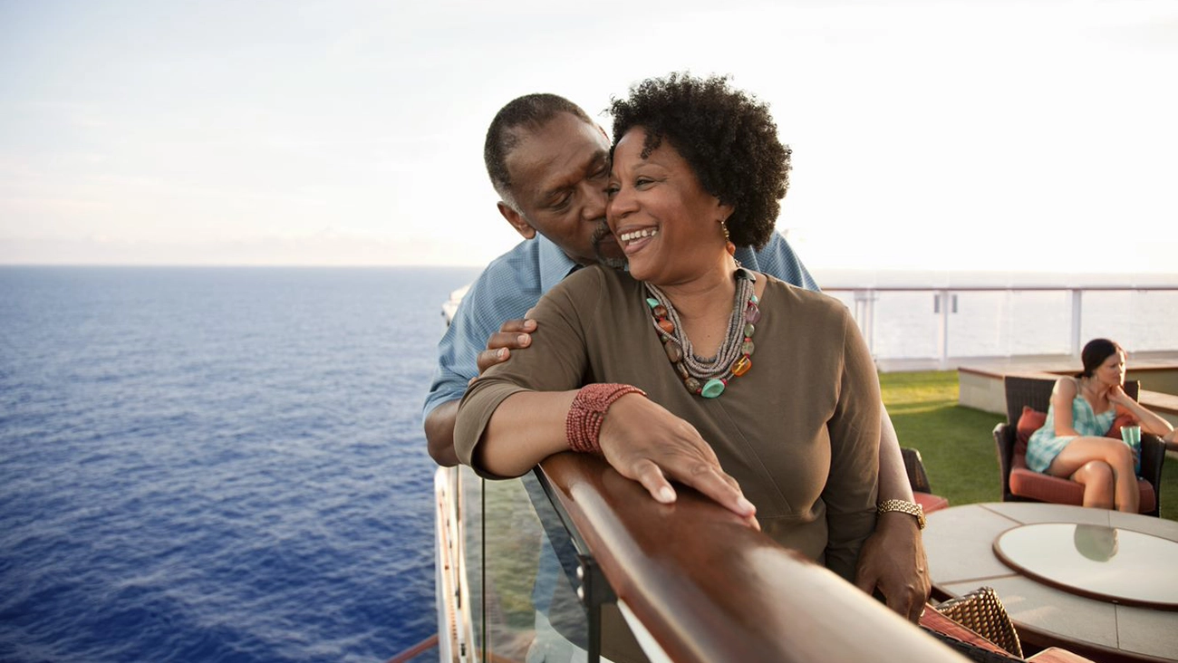 A couple enjoys each other's company on the deck of a cruise ship with the blue ocean underneath them