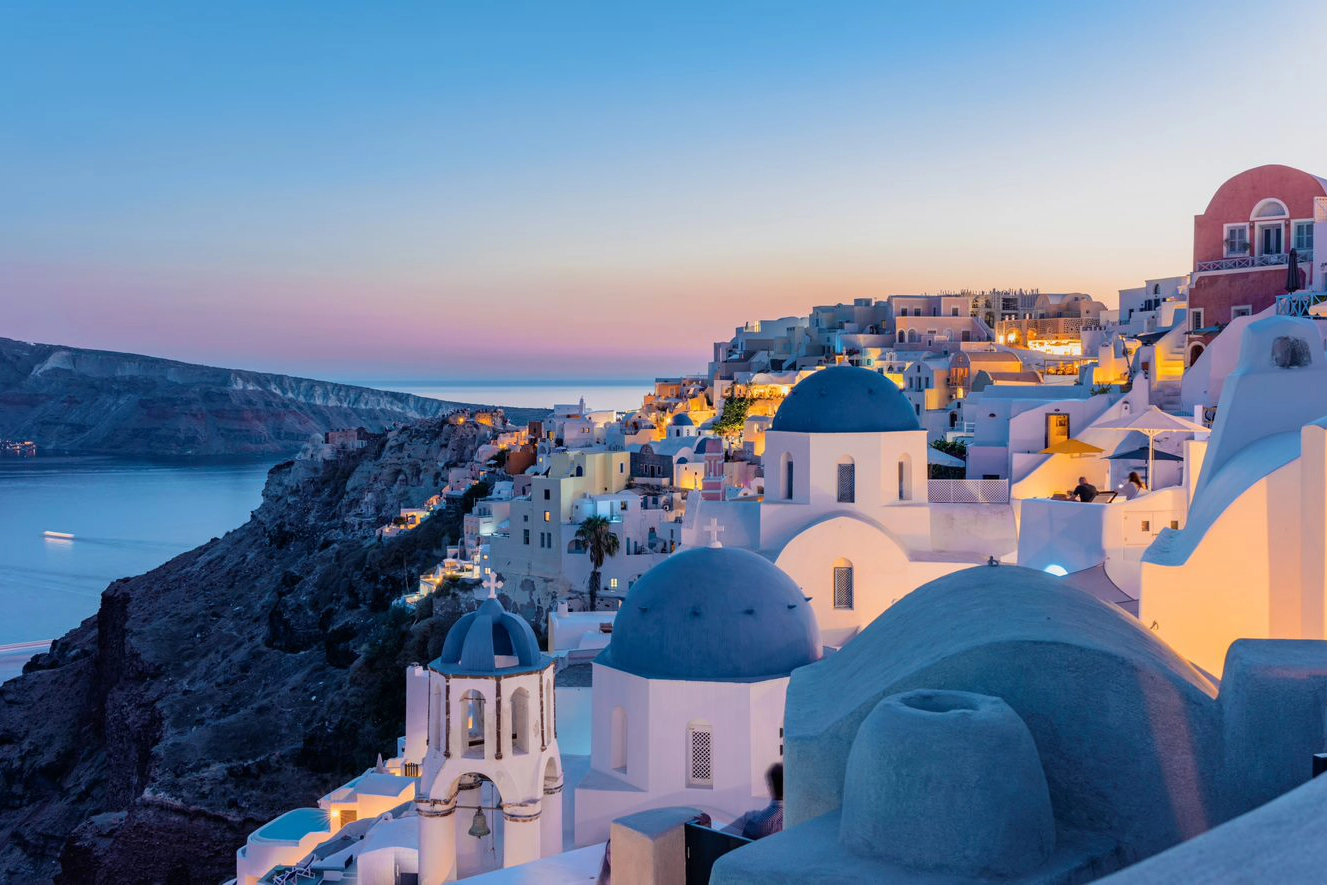White houses with blue domed roofs on hill on greek island at sunset