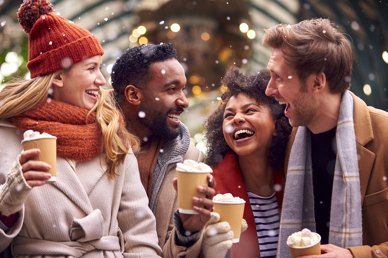 Four friends laugh and enjoy coffee together outdoors in the winter