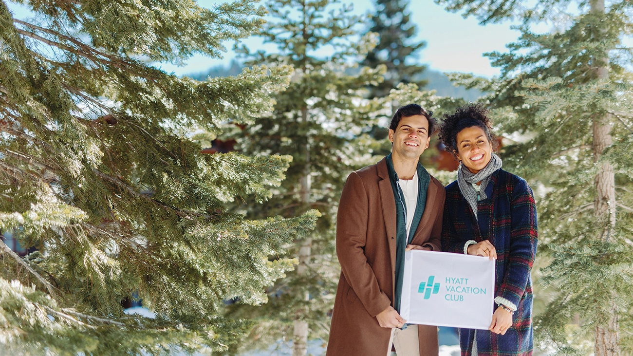 A couple holds the Hyatt Vacation Club sign outside with winter trees