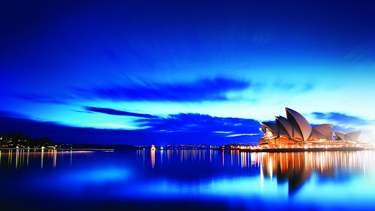 Sydney Opera House is surrounded by water at blue hour