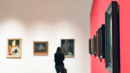 Woman looking at various framed art hangings at a museum