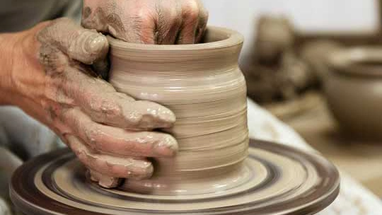 Person forming a clay pot on a potter's wheel