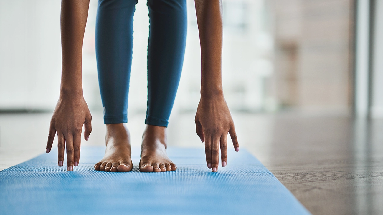 Woman in blue yoga pants stretching down to touch the floor
